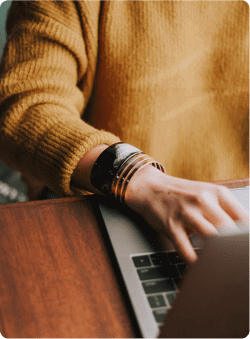 A woman, wearing a sweater and bracelets, working on a computer.