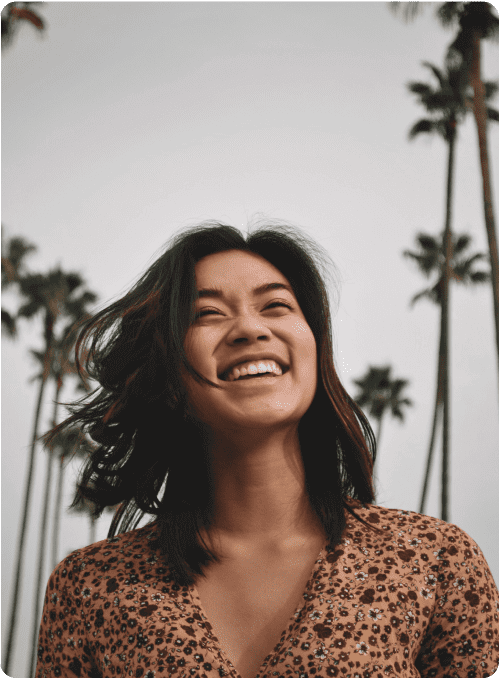 Woman laughing, standing in front of a backdrop of palm trees.